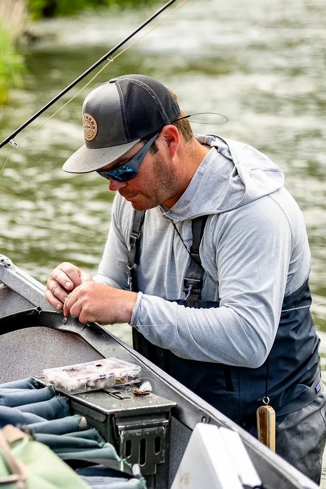 Chris O'Donnell rigging a fly at the gunwale of a drift boat on the Lower Deschutes River, fly box open beside him.